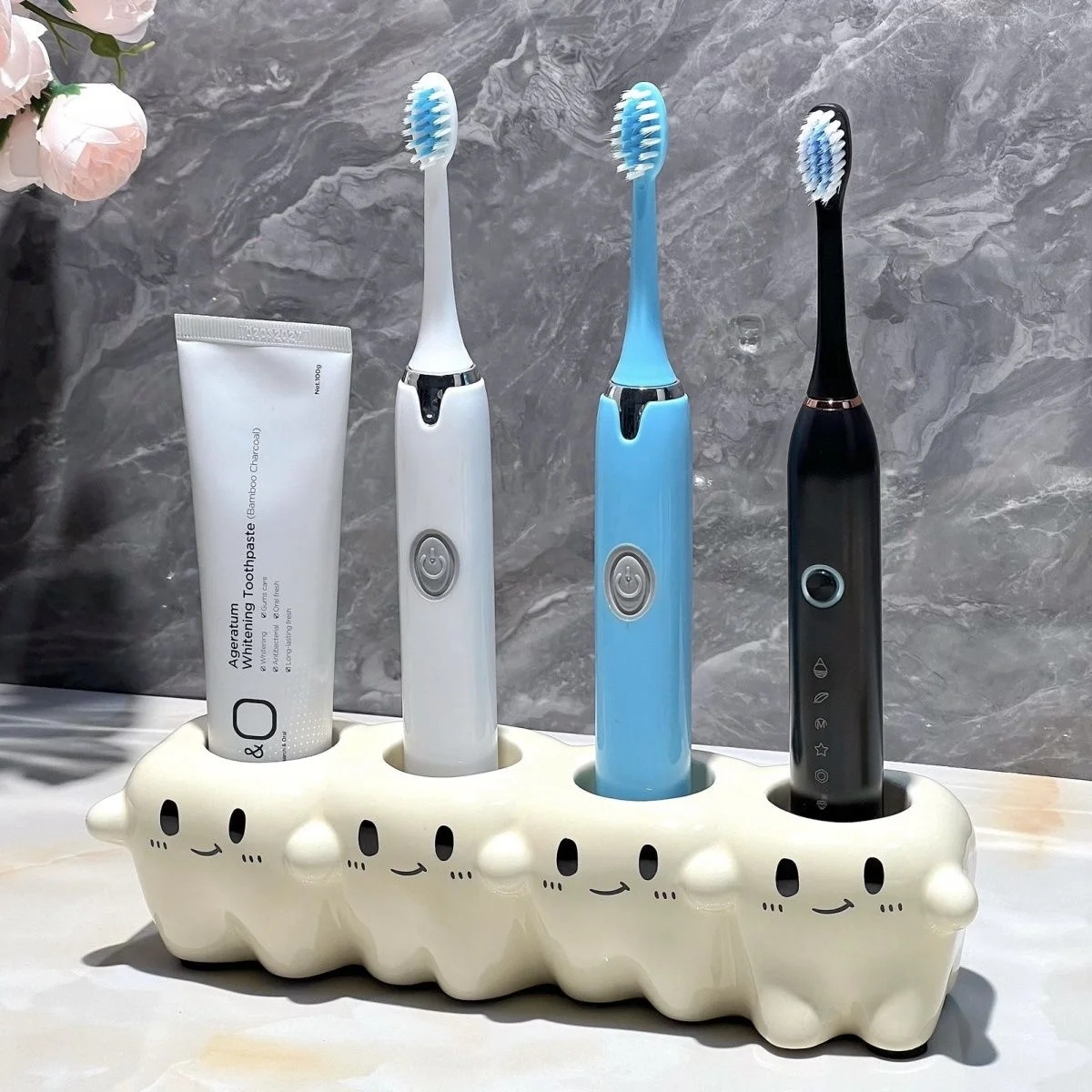 Tooth Inspired Electric Toothbrush Holder with 4 Slots Tooth-Inspired Electric Toothbrush Holder with 4 Slots holding three electric toothbrushes and one toothpaste on a marble bathroom counter.