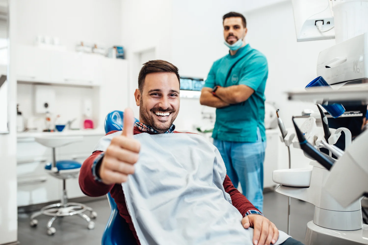 Grin Teeth About Us – Confident Patient Trusted Care Grin Teeth About Us photo: smiling patient giving thumbs up in dental clinic with dentist in background
