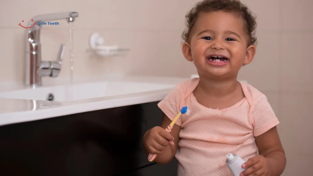 How to brush baby teeth—toddler at sink holding toothbrush and paste; smear vs pea-size fluoride, 2-minute parent-guided routine.